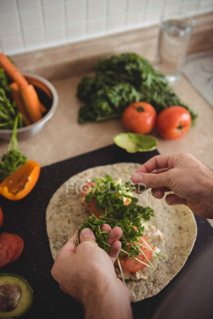 Primer plano de manos masculinas colocando hierbas en burrito en la encimera de la cocina - foto de stock