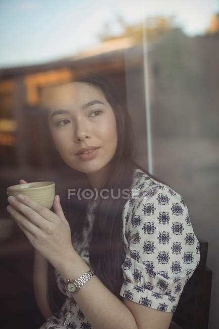 Удумлива жінка має чашку кави біля вікна в кафе — стокове фото