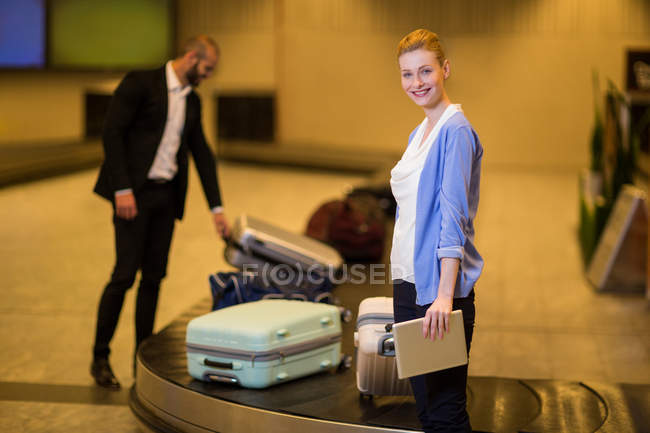Viajeros recogiendo su equipaje en el área de reclamo de equipaje en el aeropuerto - foto de stock
