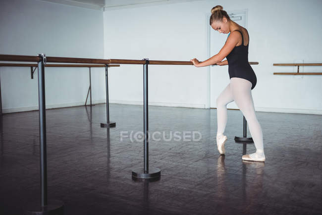 Ballerina practicing pointe at barre in ballet studio — Stock Photo
