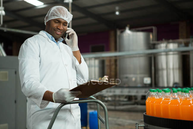 Trabajador masculino que habla por teléfono mientras examina los productos en la fábrica de jugo - foto de stock