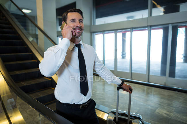 Empresario en escalera mecánica hablando por teléfono móvil en el aeropuerto - foto de stock