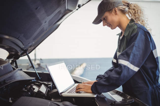 Mécanicien féminin utilisant un ordinateur portable dans le garage de réparation — Photo de stock