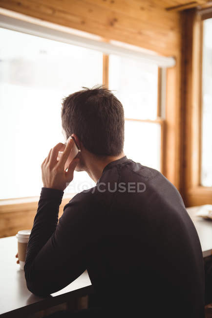Man on the phone in front of window with coffee at ski resort — Stock Photo