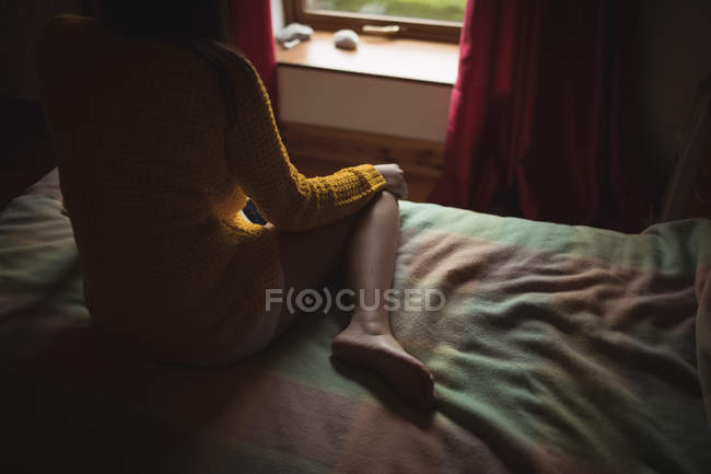 Mulher sentada na cama e olhando pela janela em casa — Fotografia de Stock