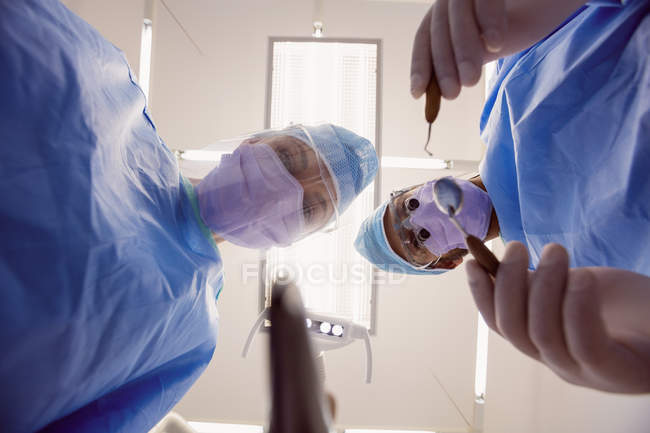 Visão de baixo ângulo de dentistas segurando ferramentas odontológicas na clínica odontológica — Fotografia de Stock