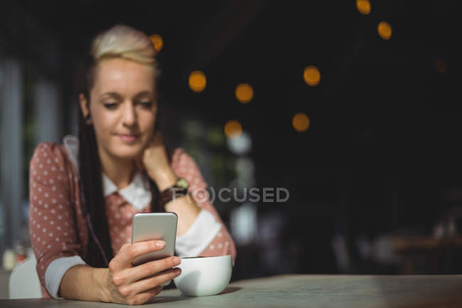 Mujer usando el teléfono móvil mientras toma café en la cafetería - foto de stock