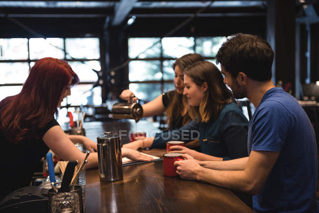 Amigos sosteniendo café en el mostrador del bar e interactuando con el camarero - foto de stock