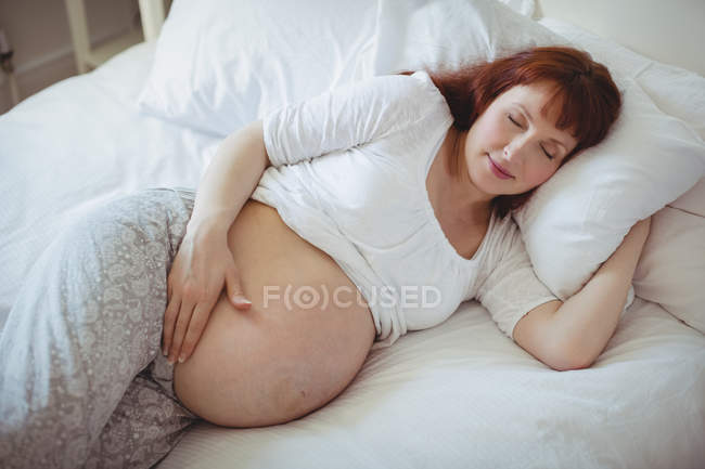 Mujer embarazada durmiendo en la cama en el dormitorio - foto de stock