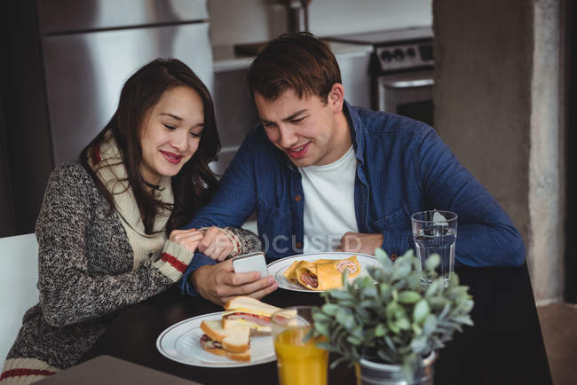Couple using mobile phone while having breakfast at home — Stock Photo