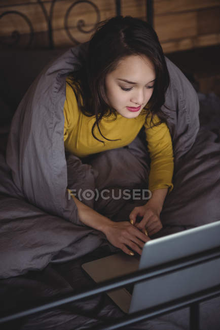 Donna sdraiata sul letto utilizzando il computer portatile in camera da letto a casa — Foto stock