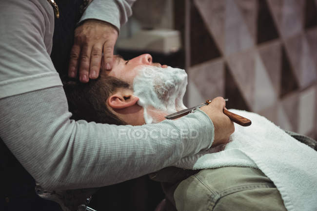 Клиент сбривает бороду бритвой в парикмахерской — стоковое фото