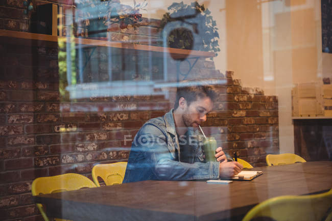 Hombre escribiendo en lácteos mientras tiene jugo en la cafetería - foto de stock