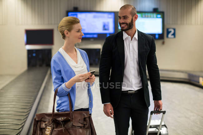 Casal sorridente andando com seus sacos de carrinho no terminal do aeroporto — Fotografia de Stock