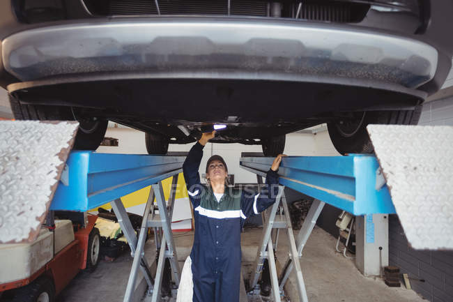 Женщина-механик осматривает автомобиль с фонариком в ремонтном гараже — стоковое фото