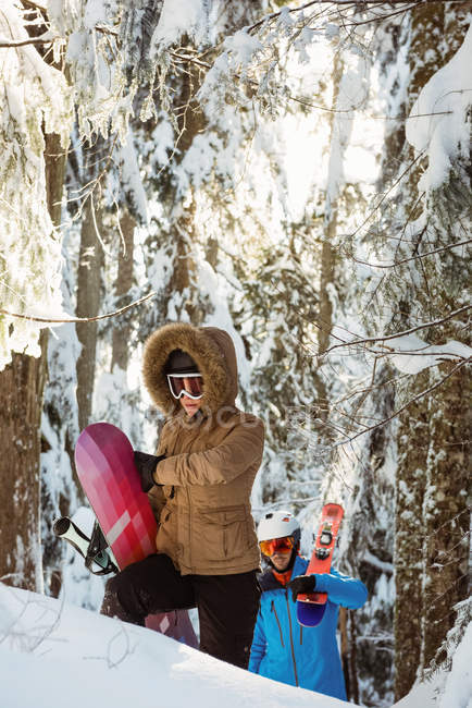 Coppia con sci e snowboard a piedi su pendio innevato — Foto stock