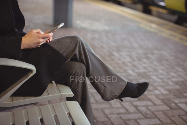 Sección media de la mujer de negocios que utiliza móvil en la plataforma en la estación de tren - foto de stock
