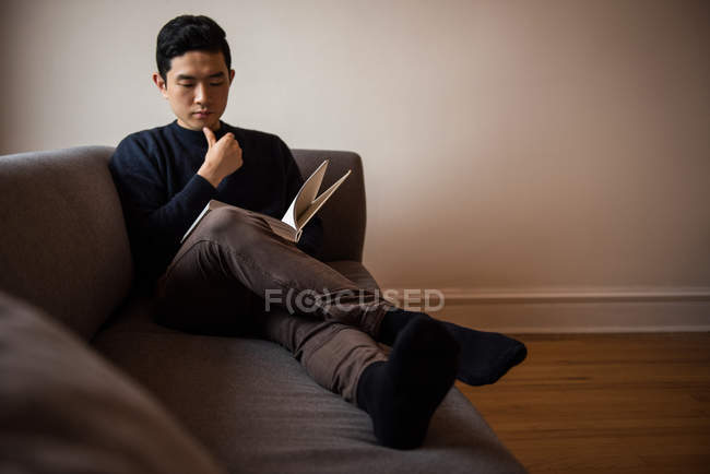Homem lendo livro na sala de estar em casa — Fotografia de Stock