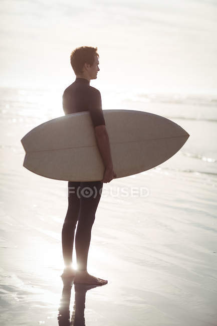 Surfista atencioso de pé com prancha na praia — Fotografia de Stock