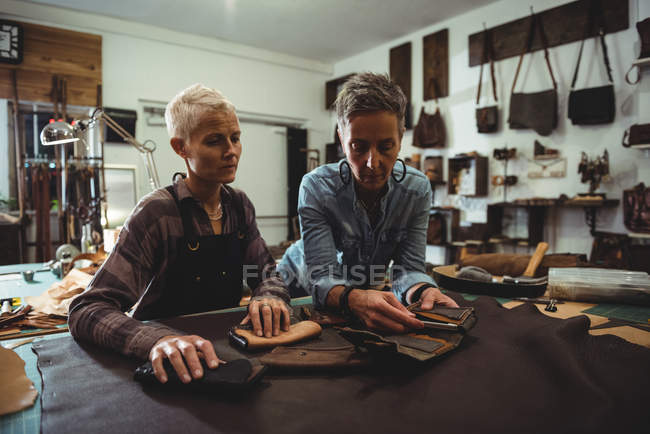 Craftswomen preparing leather cover for mobile phone in workshop — Stock Photo