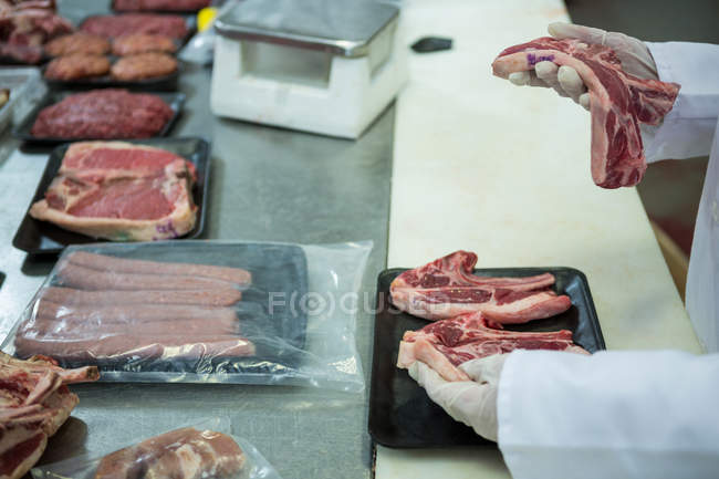Крупный план упаковки мясника сырого мяса в пластиковые упаковочные подносы на мясокомбинате — стоковое фото