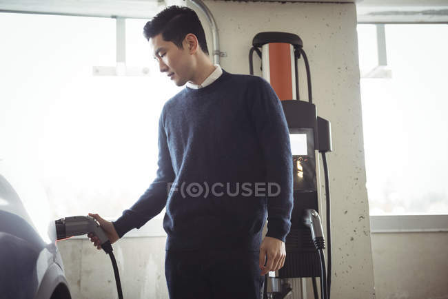 Hombre guapo que carga el coche en la estación de carga del vehículo eléctrico - foto de stock