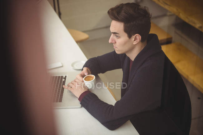 Man using laptop while having coffee in coffee shop — Stock Photo