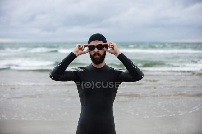 Sportler im Neoprenanzug mit Schwimmbrille am Strand — Stockfoto