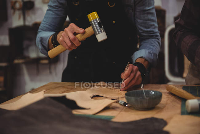 Mid-section of craftswoman hammering leather in workshop — Stock Photo