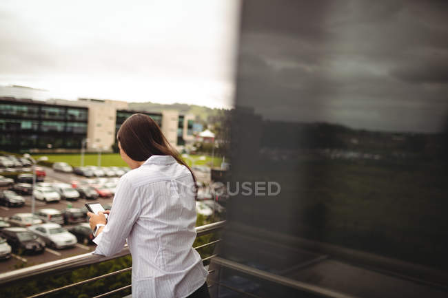 Rückansicht einer Geschäftsfrau mit Handy auf Bürobalkon — Stockfoto