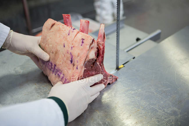 Nahaufnahme eines Metzgers, der rohes Fleisch auf Bandsägemaschine in Fleischfabrik schneidet — Stockfoto