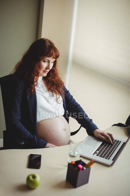 Embarazada mujer de negocios tocando el vientre mientras usa el ordenador portátil en la oficina - foto de stock