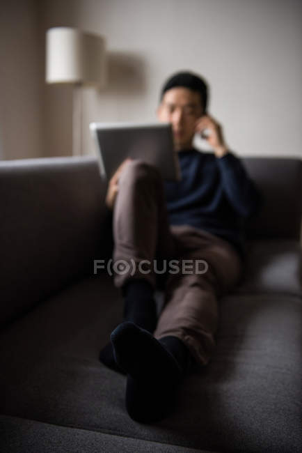 Людина розмовляє на мобільному телефоні і використовує планшет у вітальні вдома — стокове фото