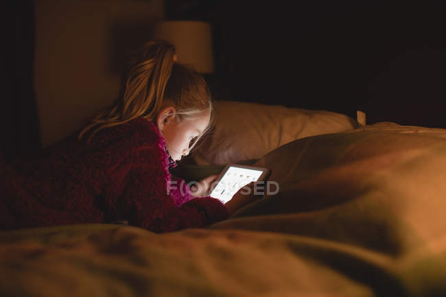 Chica sentada usando tableta digital en el dormitorio en casa - foto de stock
