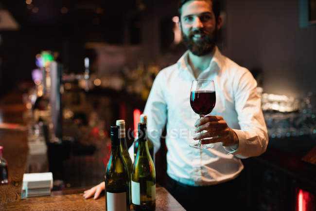 Portrait of bartender holding glass of red wine at bar counter — Stock Photo