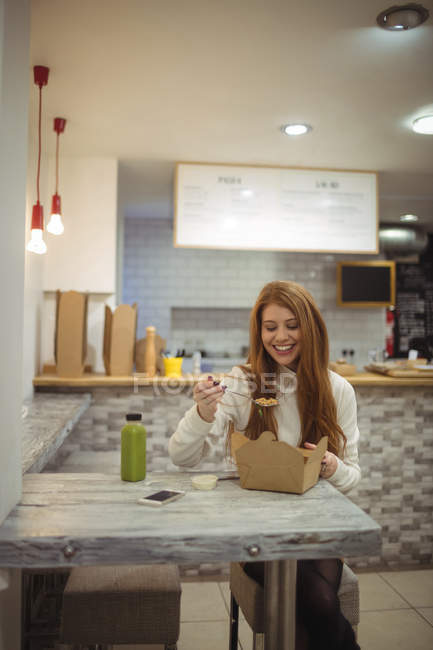 Jovem mulher sorrindo enquanto come salada no restaurante — Fotografia de Stock