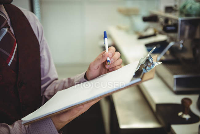 Mid section of man looking at clipboard in coffee shop — Stock Photo