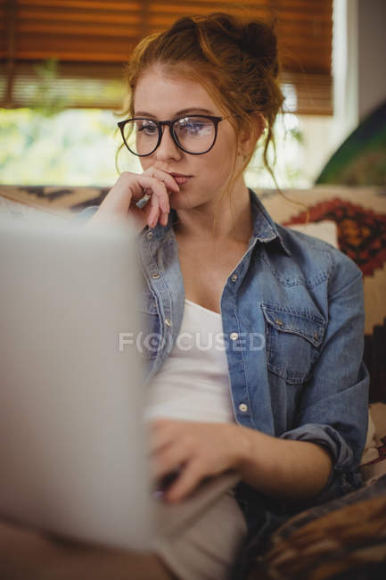 Mujer reflexiva usando el ordenador portátil en casa - foto de stock