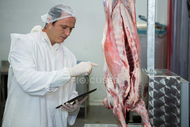 Carniceiro macho mantendo registros em tablet digital na fábrica de carne — Fotografia de Stock