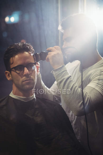 Man getting hair trimmed by barber with trimmer in barber shop — Stock Photo
