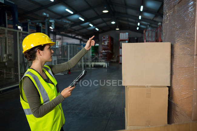 Trabajadora usando tableta digital mientras trabaja en fábrica - foto de stock