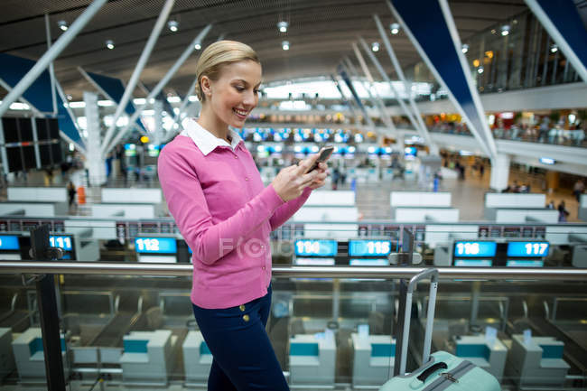 Comutador feminino com bagagem usando telefone celular no aeroporto — Fotografia de Stock