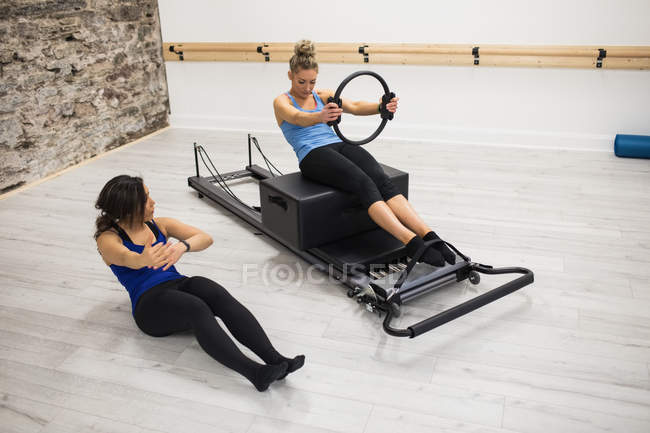 Entraîneur féminin aidant femme avec l'exercice avec anneau pilates dans la salle de gym — Photo de stock