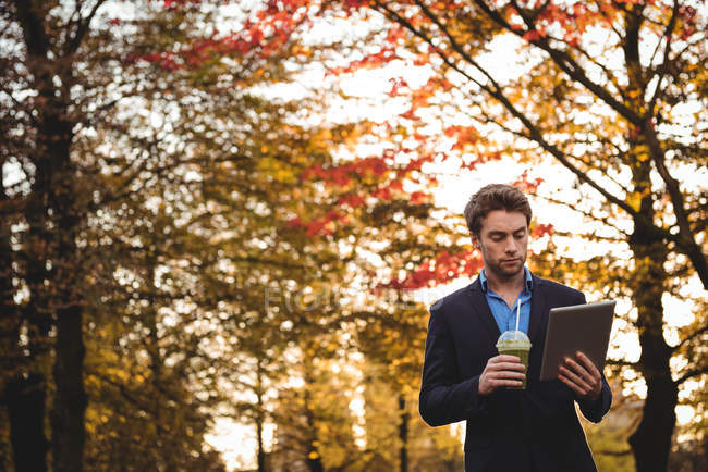 Businessman using digital tablet while having juice in autumn — Stock Photo