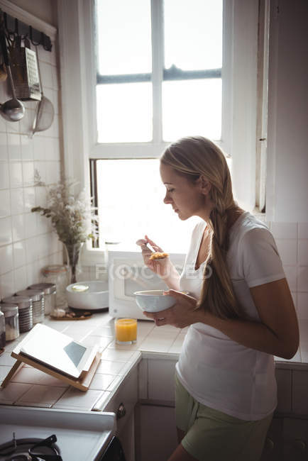 Женщина завтракает, глядя на цифровой планшет на кухне дома — стоковое фото