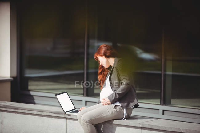 Embarazada mujer de negocios utilizando ordenador portátil en las instalaciones de la oficina - foto de stock