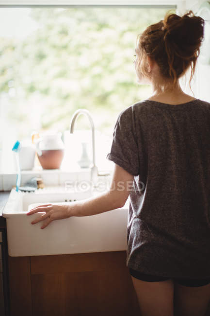 Visão traseira da mulher olhando através da janela em casa — Fotografia de Stock