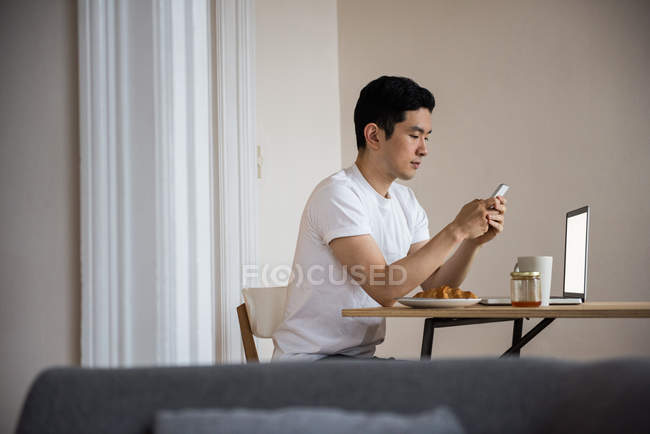Mann benutzt Handy, während er zu Hause eine Tasse Kaffee trinkt — Stockfoto