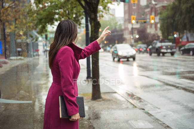 Businesswoman hailing a taxi cab from city street sidewalk — Stock Photo