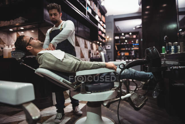 Barbeiro colocando toalha sobre o cliente na barbearia — Fotografia de Stock